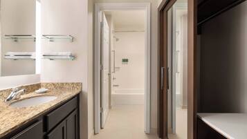 A modern bathroom with a granite countertop sink, a large mirror, and a walk-in shower.