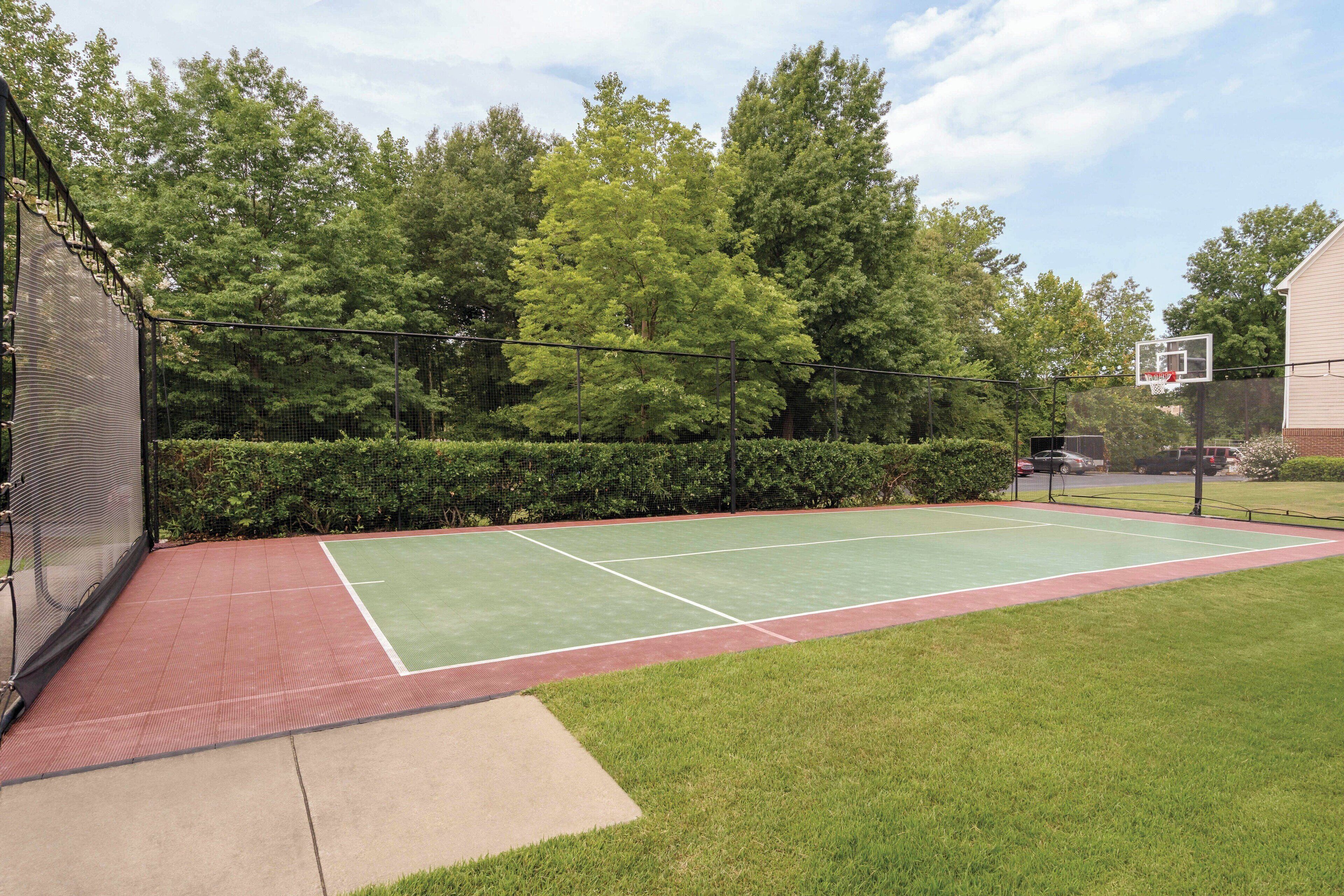 An outdoor tennis court with a net, surrounded by a fence and trees.