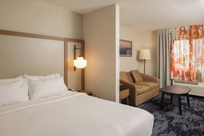 A hotel room with a large bed, a sofa, a small table, a lamp, and a window with curtains. - Fairfield Inn & Suites Lansing West (Lansing)
