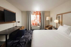 A hotel room with a bed, desk, chair, TV, air conditioning unit, and a lamp. - Fairfield Inn & Suites Lansing West (Lansing)