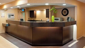 A reception desk with a digital display, a clock, and a vase with a plant. - Residence Inn Lansing West (Lansing)