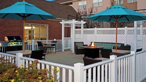 An outdoor patio with seating and a grill area, enclosed by a white fence and featuring two large umbrellas. - Residence Inn Lansing West (Lansing)