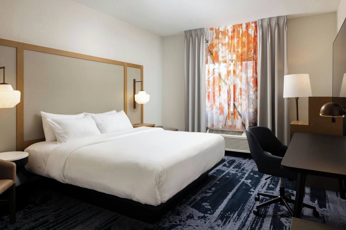 A hotel room with a large bed, a desk, a chair, and a window with curtains.