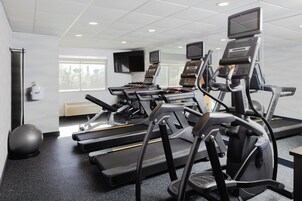 Un gimnasio con cintas de correr, pelotas de ejercicios y una pantalla de televisión.