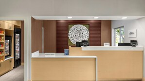 A hotel reception desk with a wooden panel wall, a large circular wall art piece, and a minibar area with snacks. - Fairfield Inn & Suites Saginaw (Saginaw)