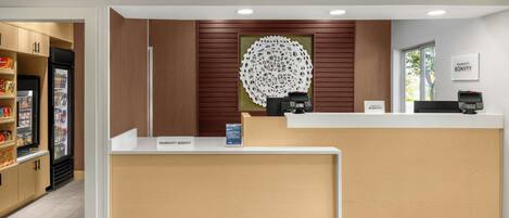 Un comptoir d’accueil d’hôtel avec une plaque nominative, un élément décoratif mural et un distributeur automatique.