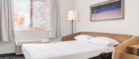 A hotel room with a bed, a desk, a lamp, and a painting on the wall.