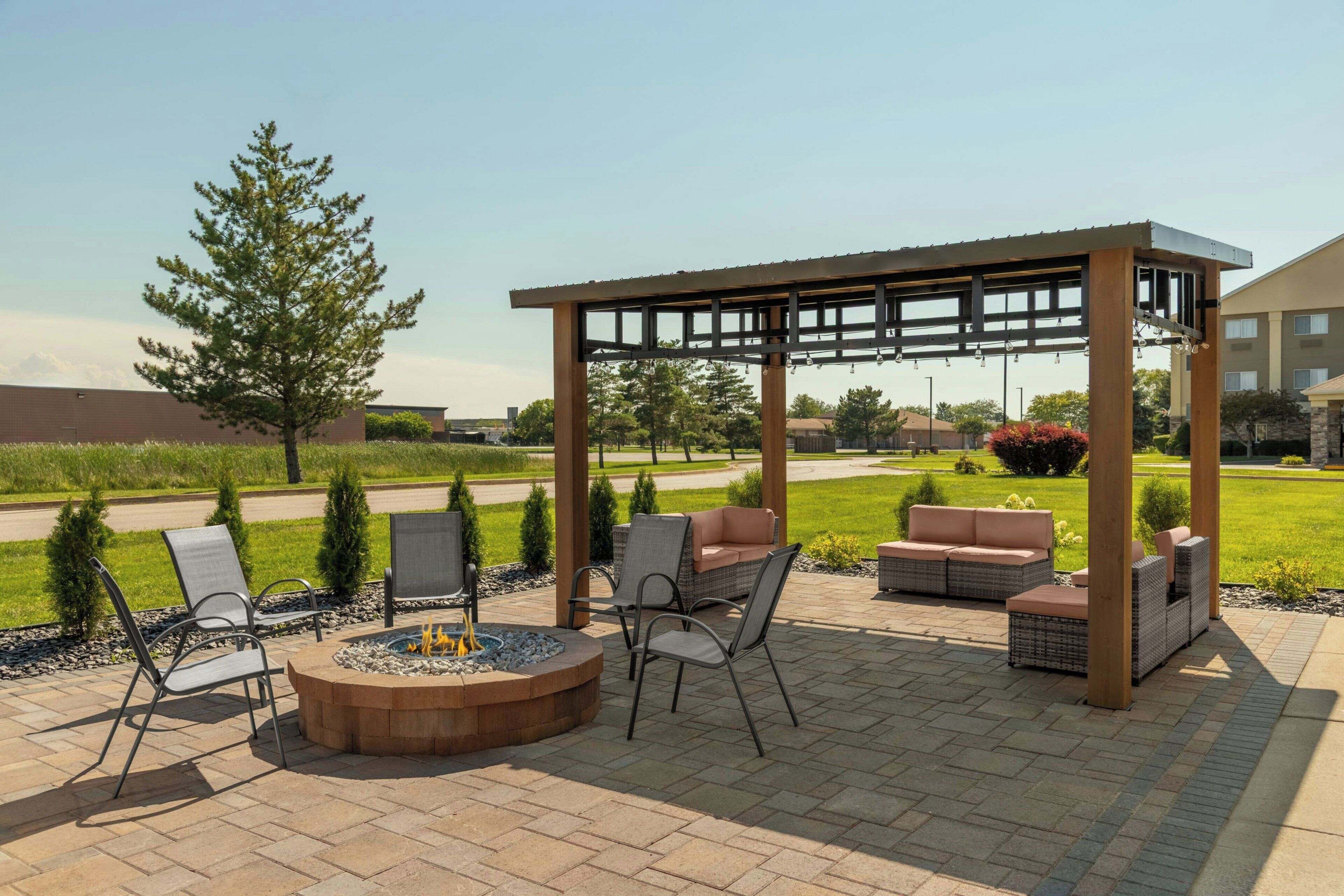 An outdoor patio area with a fire pit, seating, and a pergola structure.