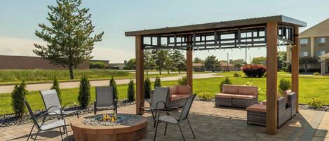 An outdoor patio area with a fire pit, seating, and a pergola structure.