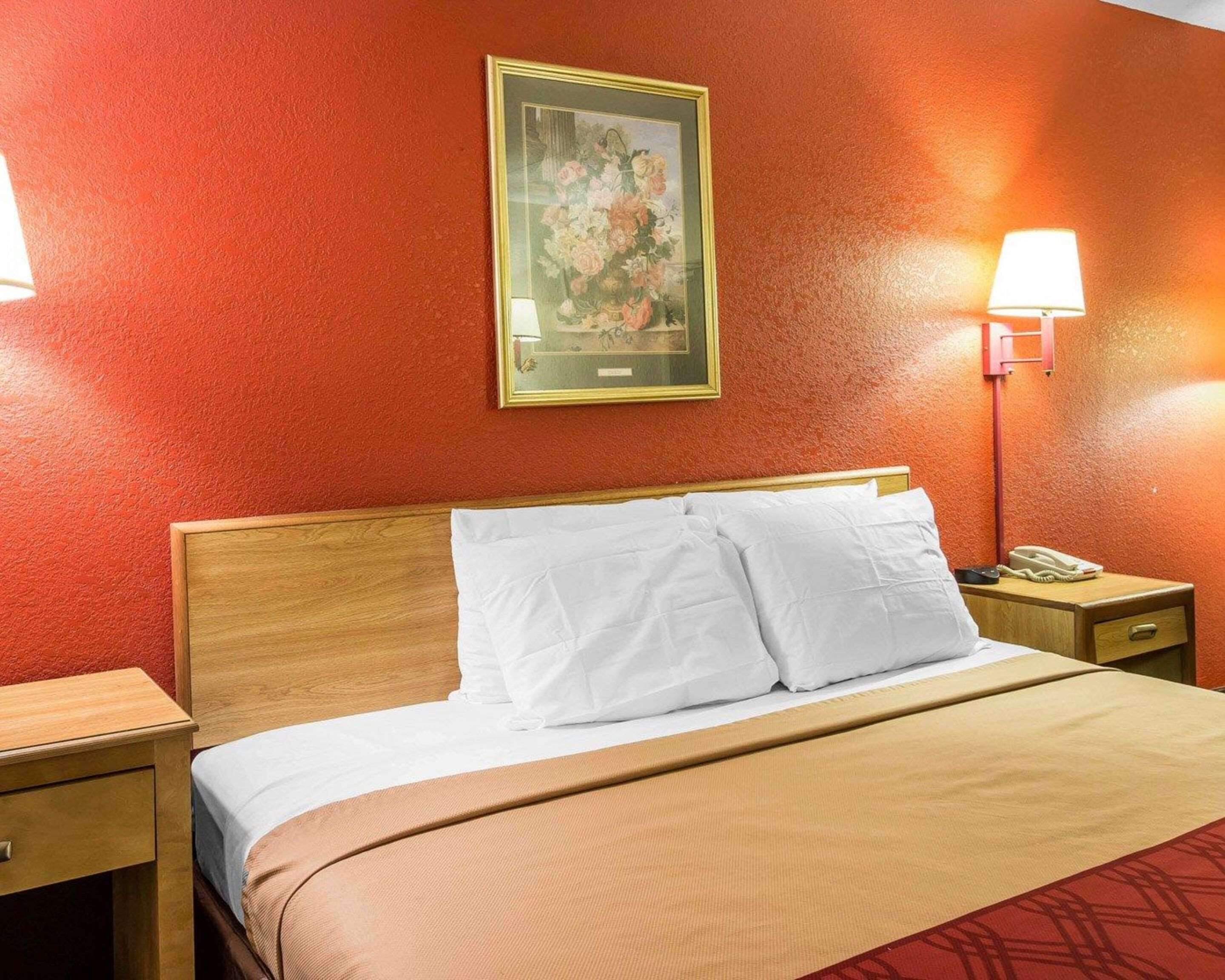 Habitación de hotel con cabecera de madera, ropa de cama blanca, una obra de arte floral enmarcada en la pared y lámparas de noche.