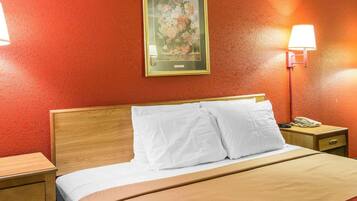 Habitación de hotel con cabecera de madera, ropa de cama blanca, una obra de arte floral enmarcada en la pared y lámparas de noche.