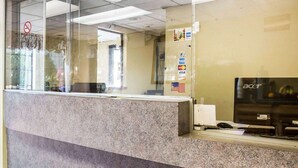 Un mostrador de recepción con computadora y monitor, una alfombra roja y un cartel de prohibido fumar.