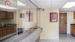 Un vestíbulo de hotel con mostrador de recepción, un cartel de prohibido fumar, un anuncio enmarco para el desayuno continental 'Easy Starts' y una puerta de madera que indica un baño.