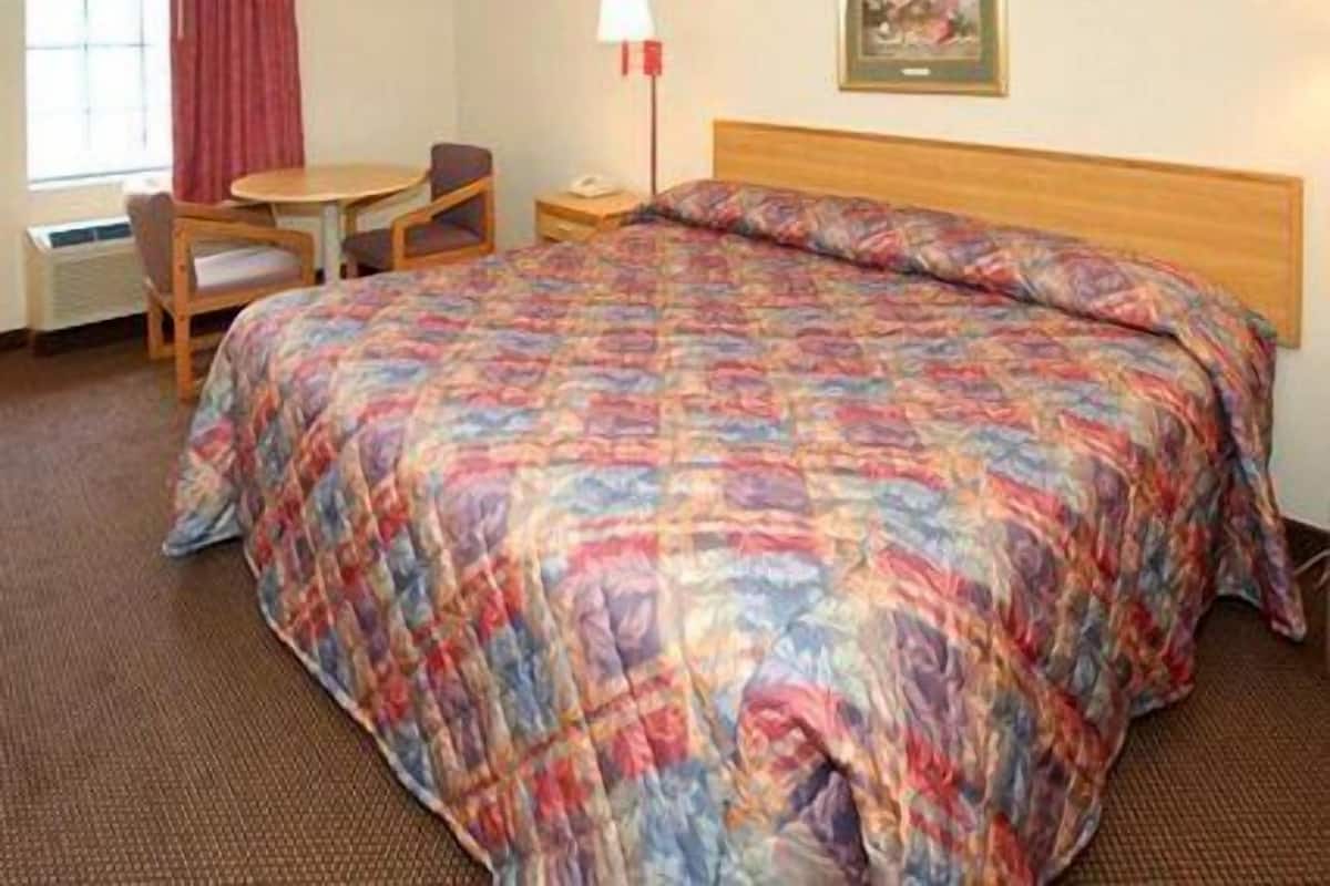 A hotel room with a large bed, a small round table, a chair, a lamp, and a window with curtains.