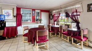 Un coin repas comprenant une table ronde et six chaises, un four à micro-ondes, un évier et une fenêtre avec des rideaux.