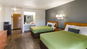 Une chambre d’hôtel avec deux lits, un bureau, un miroir et une table de chevet avec des lampes.
