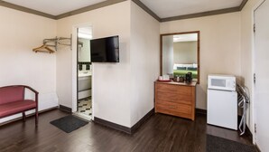 Une chambre d’hôtel avec un plancher en bois, un canapé rouge, un téléviseur fixé au mur, une commode en bois, un four à micro-ondes et un miroir.
