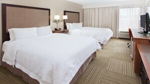 Habitación de hotel con dos camas, un escritorio, un televisor y una ventana con cortinas.