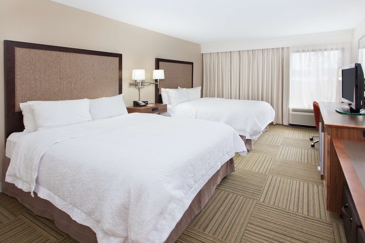 A hotel room with two beds, a desk, a television, and a window with curtains.