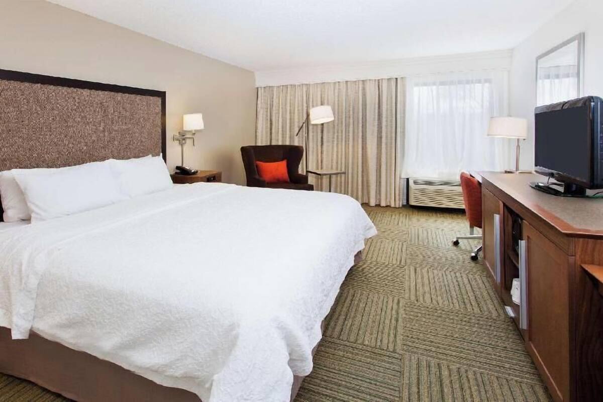 A hotel room with a large bed, a desk with a television, a chair, and a lamp.