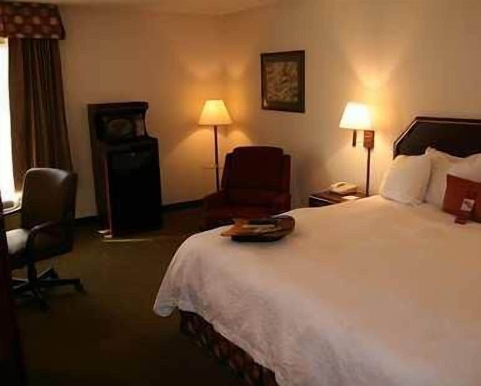 Een hotelkamer met een groot bed, twee bedlampen, een stoel, een bureau en een klok.