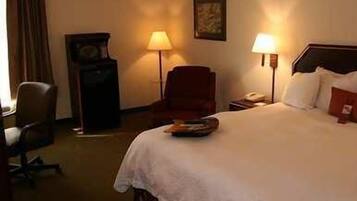 Een hotelkamer met een groot bed, twee bedlampen, een stoel, een bureau en een klok.