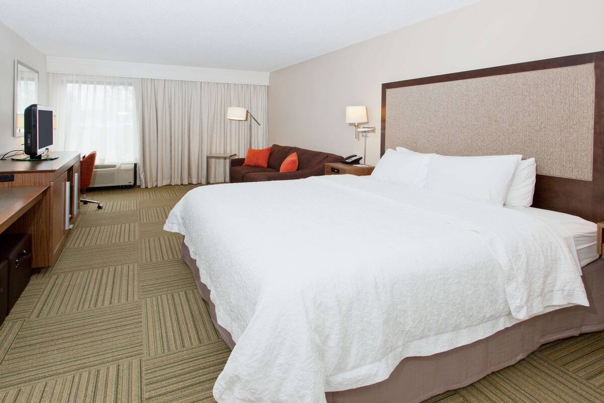A hotel room with a large bed, a desk with a computer, a chair, a lamp, and a telephone.