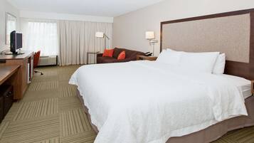 Una habitación de hotel con una cama grande, un escritorio con computadora, una silla, una lámpara y un teléfono.