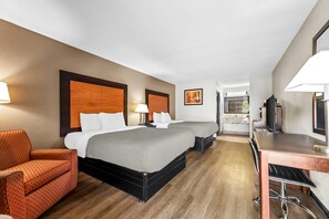 A hotel room with two beds, a desk, a chair, and a TV.