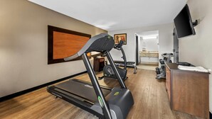A hotel room with a treadmill, a desk, a flat-screen TV, and a painting on the wall. - Quality Inn Richland - Jackson South (Richland)