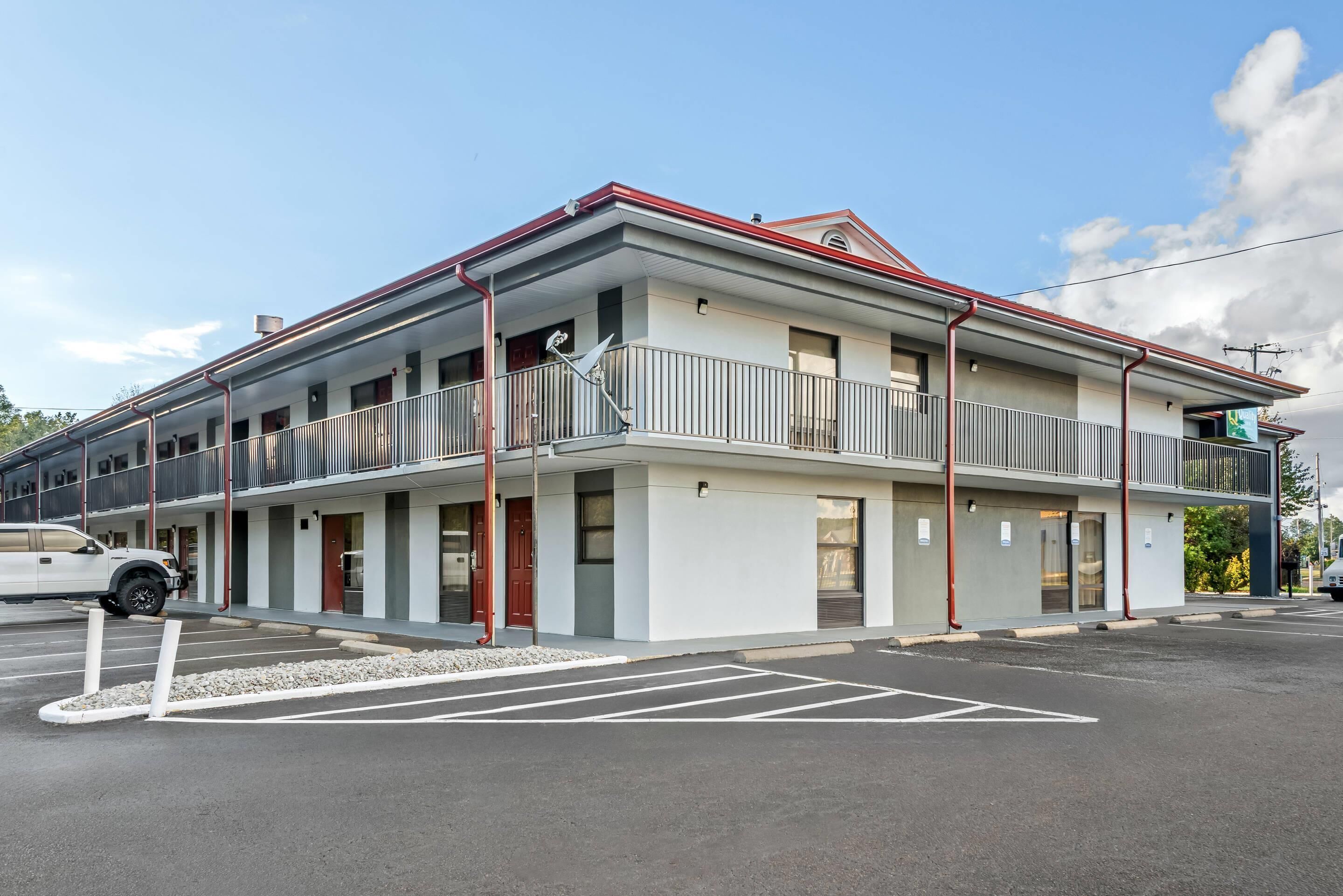 Motel de dues plantes amb teulada plana, un balcó al segon pis i un aparcament al davant.
