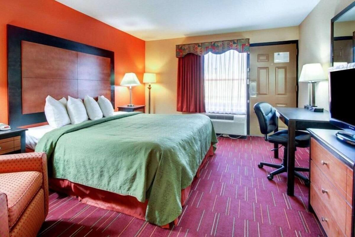 A hotel room with a bed, desk, chair, and a television.