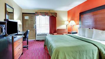 Habitación de hotel con cama, escritorio con televisor, silla, lámpara de escritorio y ventana con cortinas.
