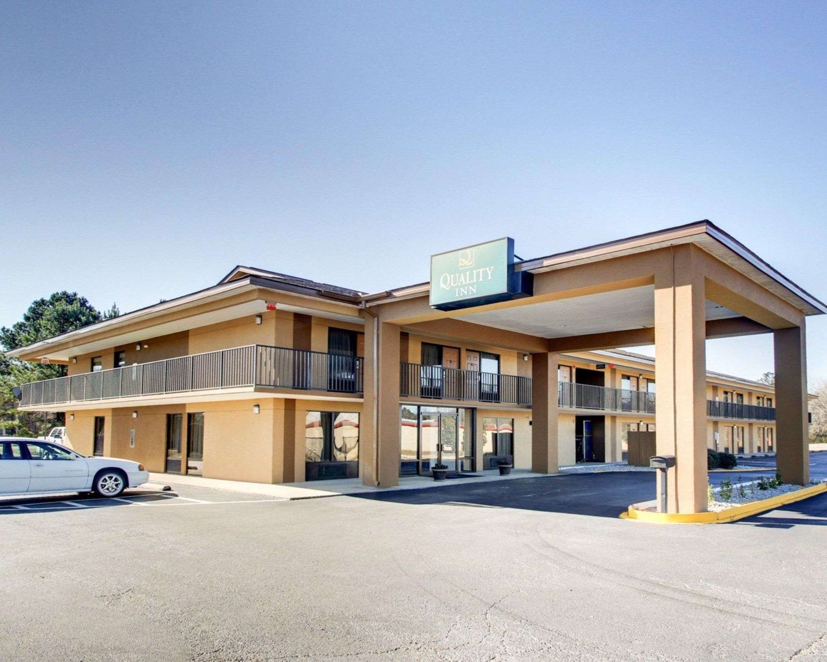Ein zweistöckiges Motel mit überdachtem Parkplatz und einem Schild mit der Aufschrift 'Quality Inn'.