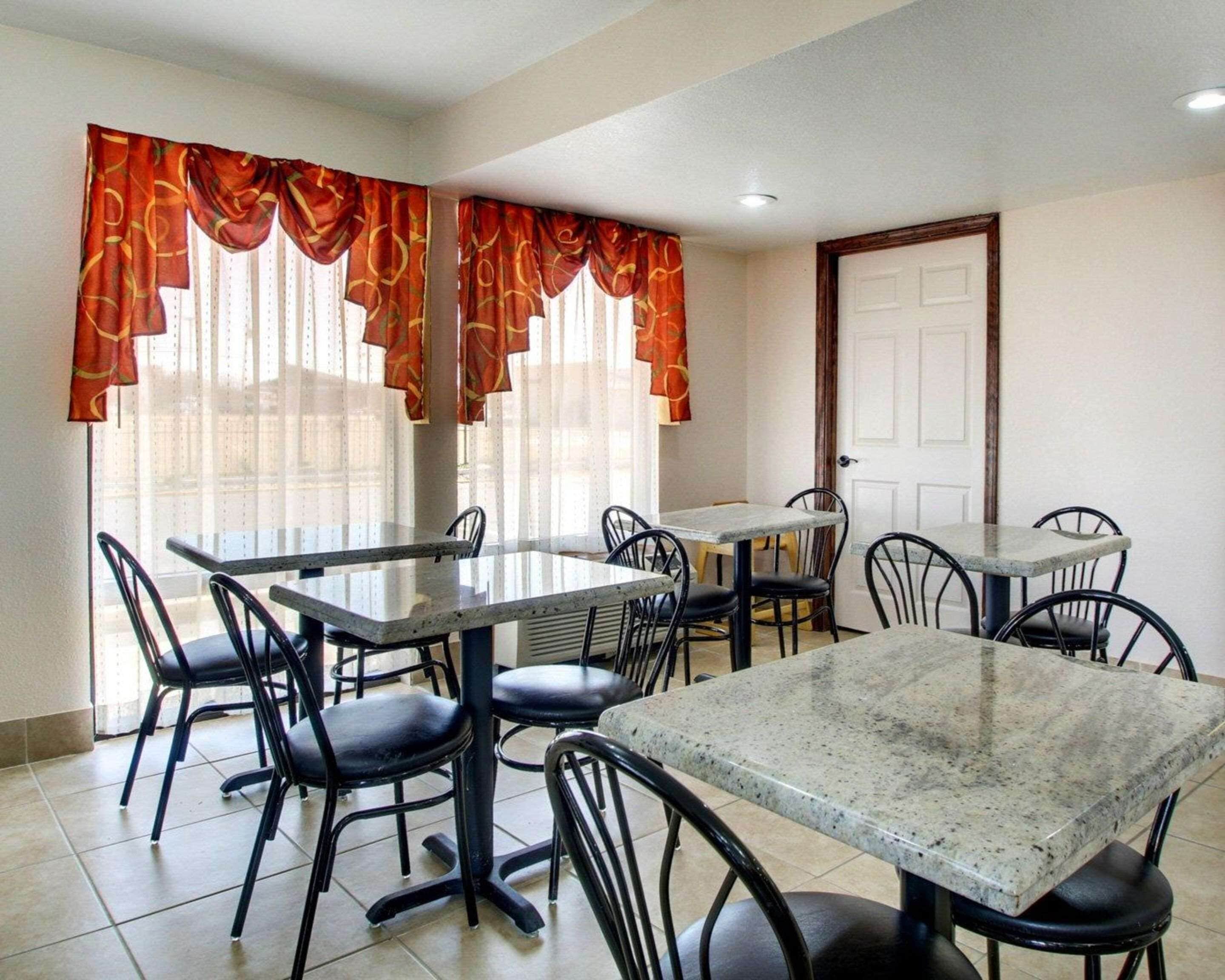 Un comedor con mesas y sillas, ventanas amplias con cortinas, y una puerta.