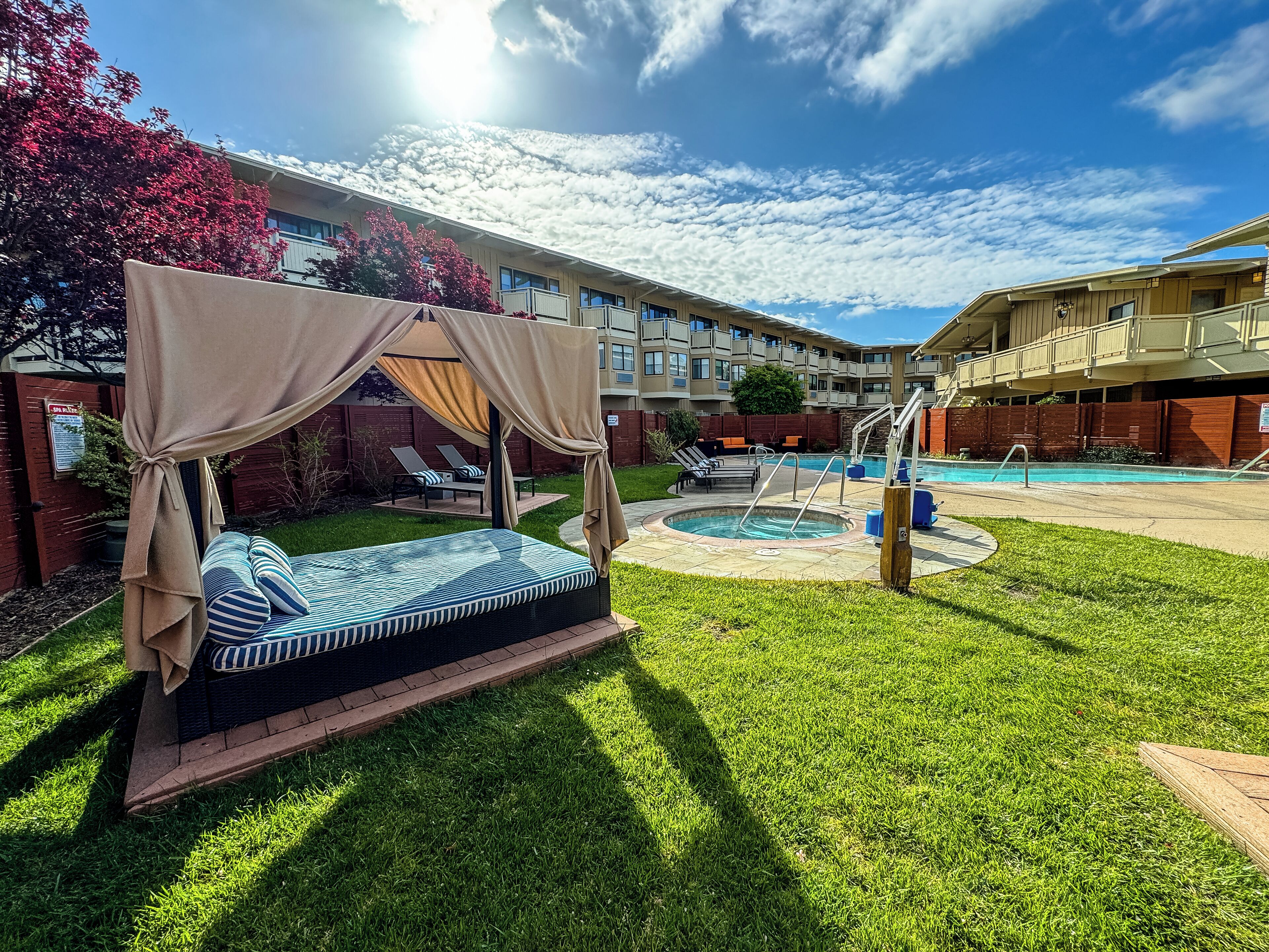 A well-maintained outdoor pool area with a canopy bed, lounge chairs, and a clear view of the building in the background.