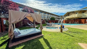 A well-maintained outdoor pool area with a canopy bed, lounge chairs, and a clear view of the building in the background.