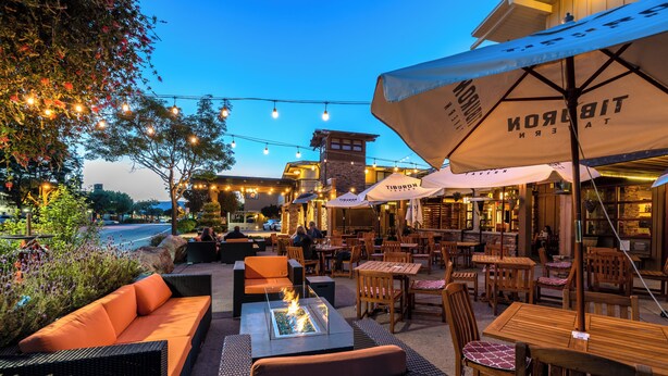 An outdoor seating area with wicker furniture, a fire pit, and umbrellas branded with "Tiburon."