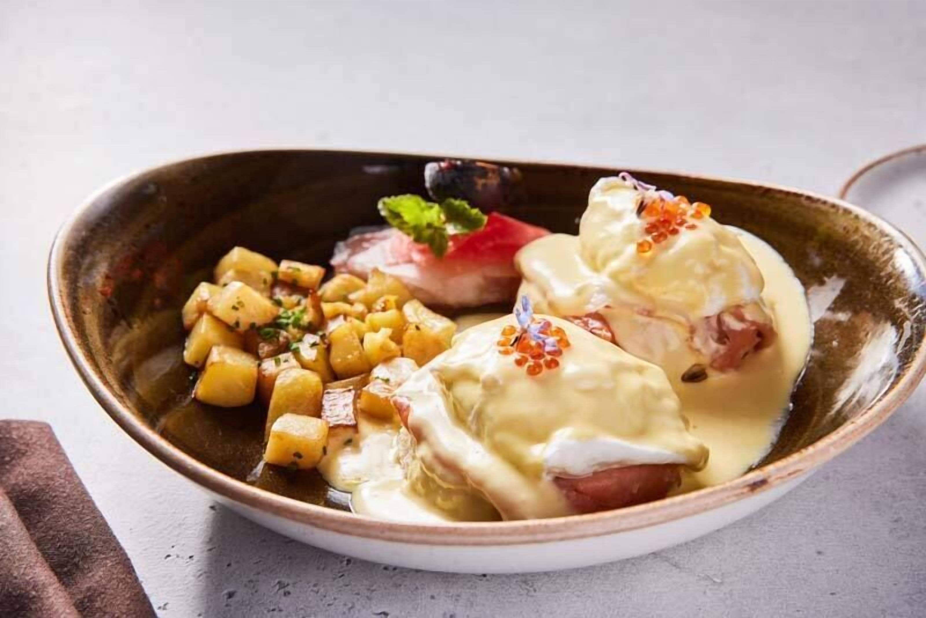 Un plato con huevos pochados, patatas y una guarnición de fruta roja en un cuenco de cerámica.