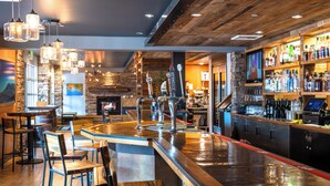 A bar area with multiple seating options, a counter with a cash register, and a variety of bottles on shelves.