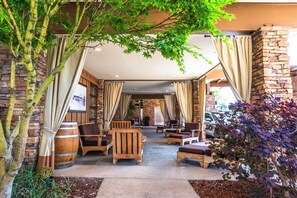 A covered outdoor seating area with stone walls, wooden furniture, and a large barrel. - The Lodge at Tiburon (Tiburon)