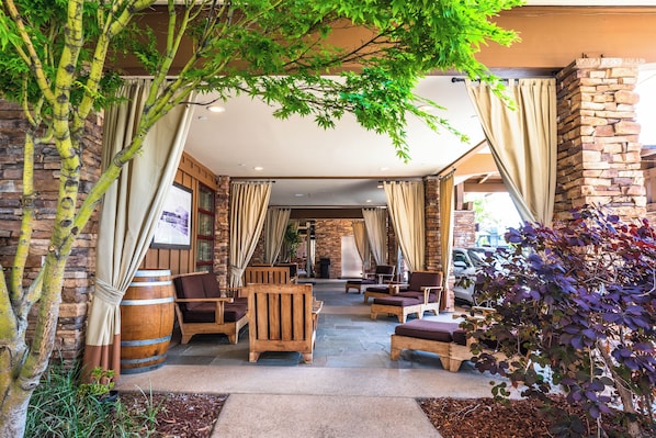 A covered outdoor seating area with stone walls, wooden furniture, and a large barrel.