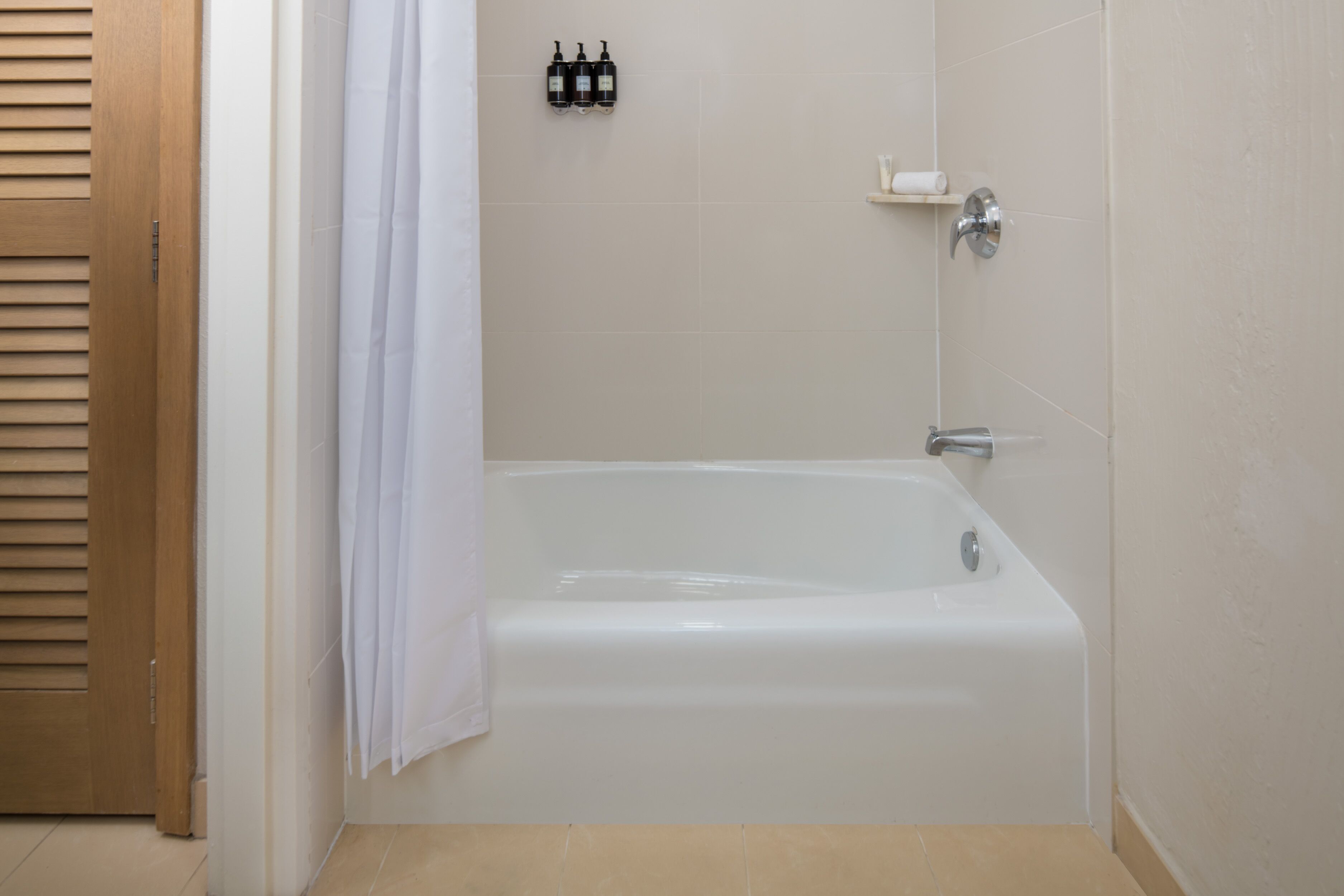 A bathroom with a bathtub, a shower curtain, and a shelf with toiletries.