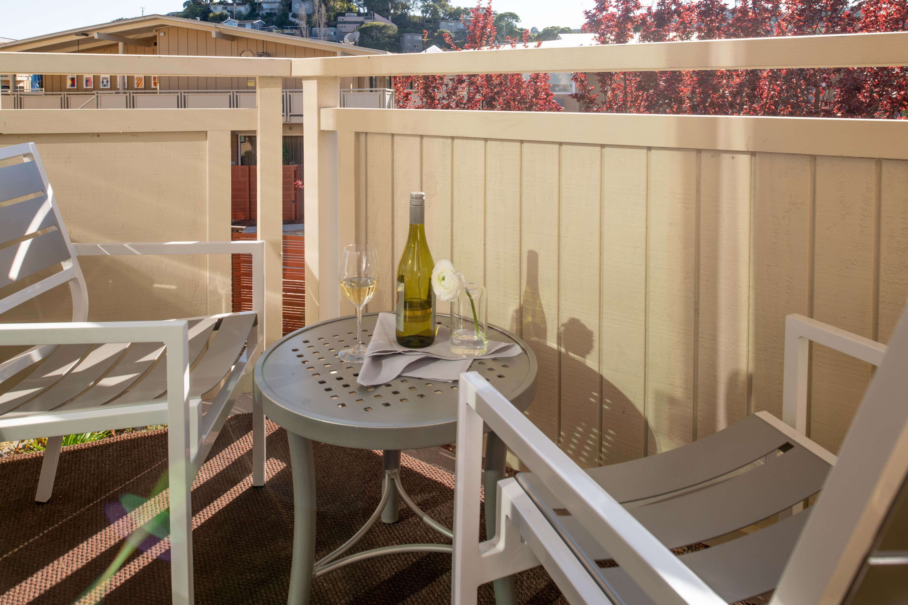 En balkon med et bord og to hvide stole, en vinflaske og et glas på bordet.