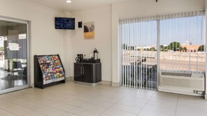 Et receptionsområde med kaffeinstallation, en glasdørindgang, en opslagstavle og et stort vindue med persienner.