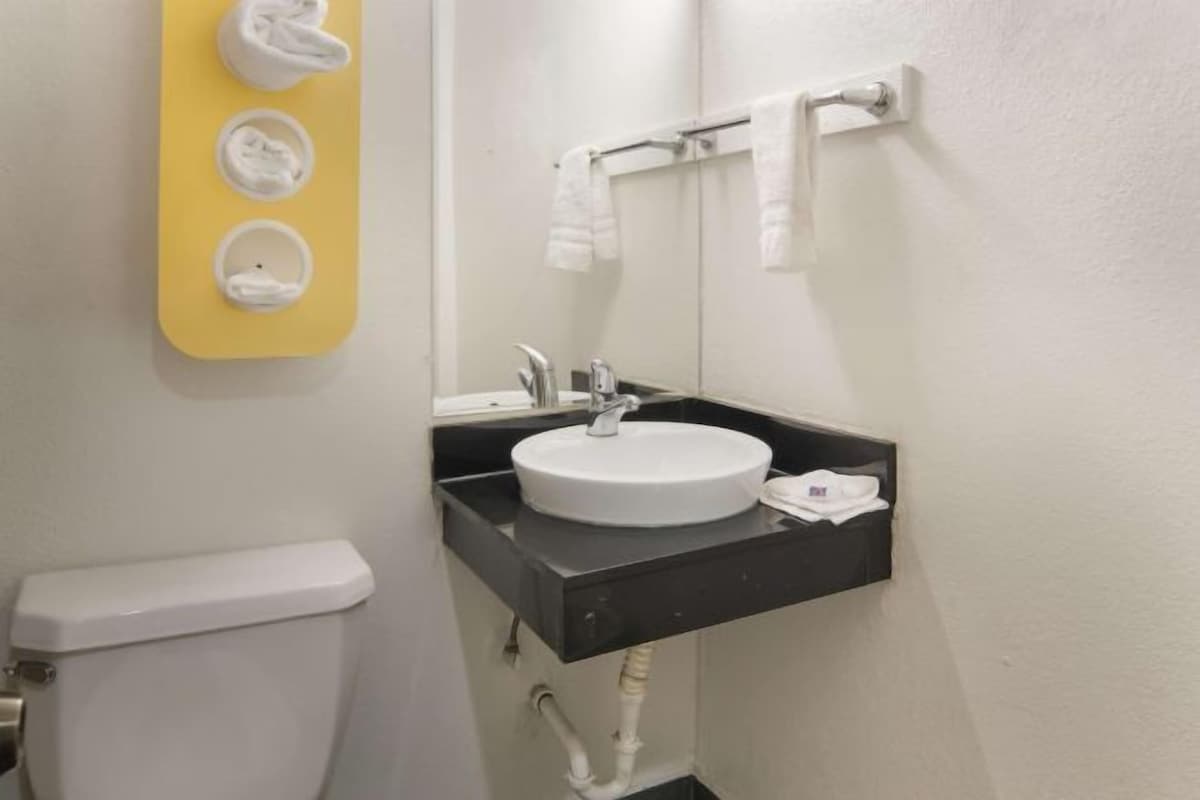 A bathroom with a white toilet, a sink with a mirror, and a towel rack with towels.