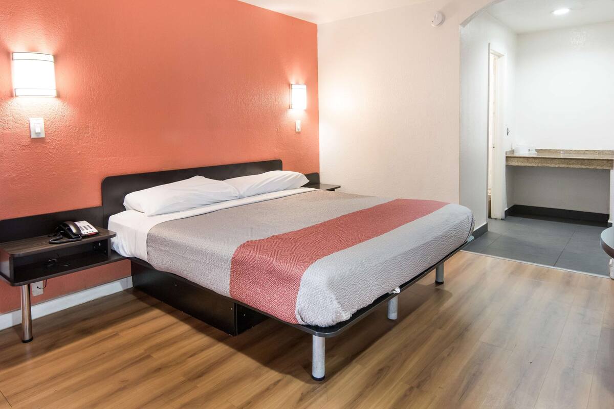 A hotel room with a bed, bedside table, and a desk area.