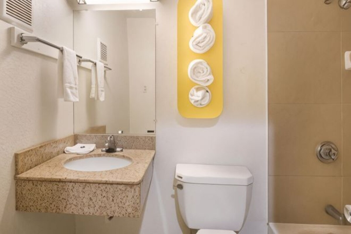 Un baño con lavamanos de encimera de granito, inodoro y toallero con toallas dobladas.