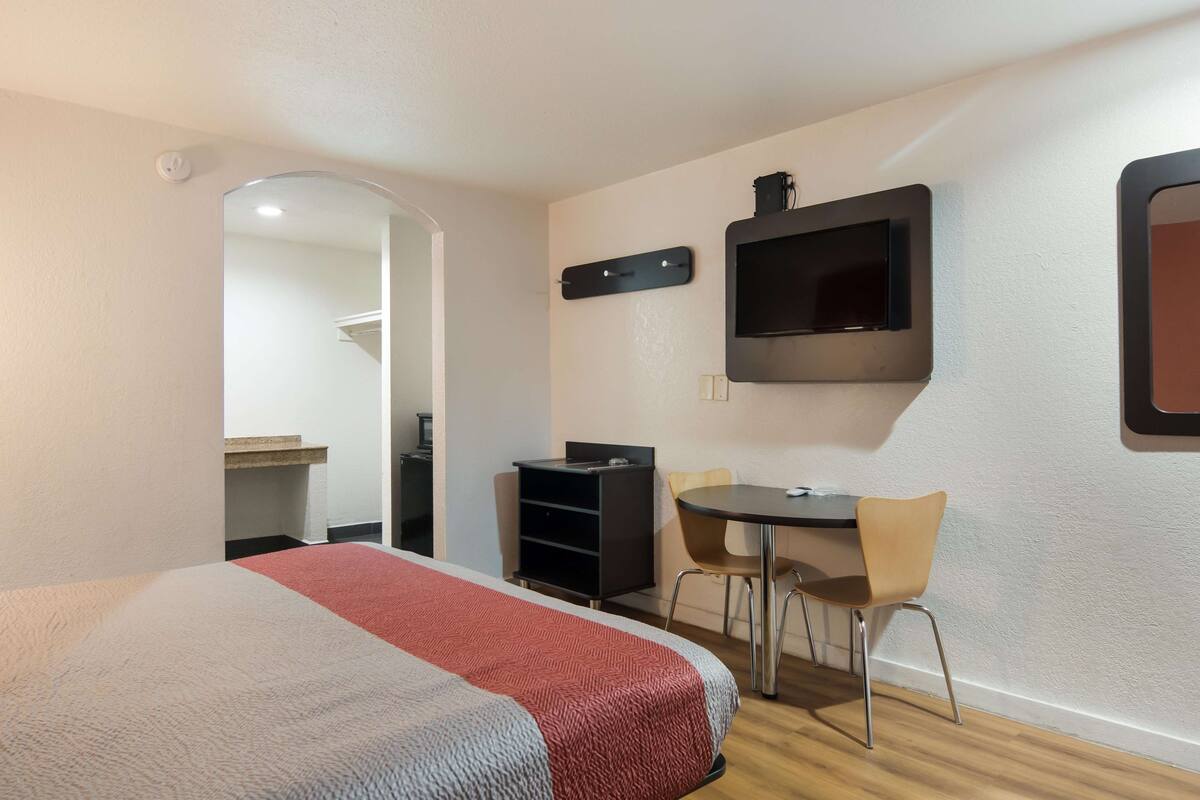 A hotel room with a bed, a desk, two chairs, a TV, and a mirror.
