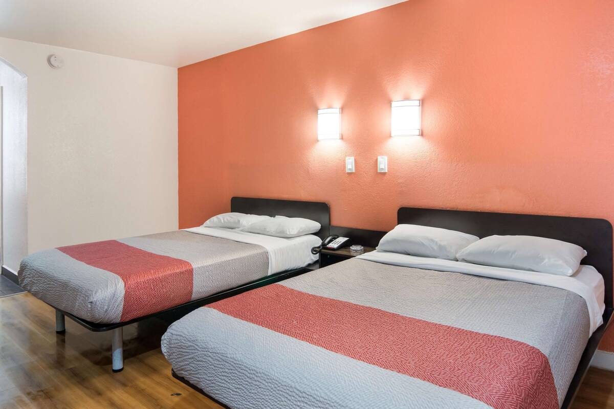 A hotel room with two single beds, each with a red and white bedspread, and a small bedside table with a phone.